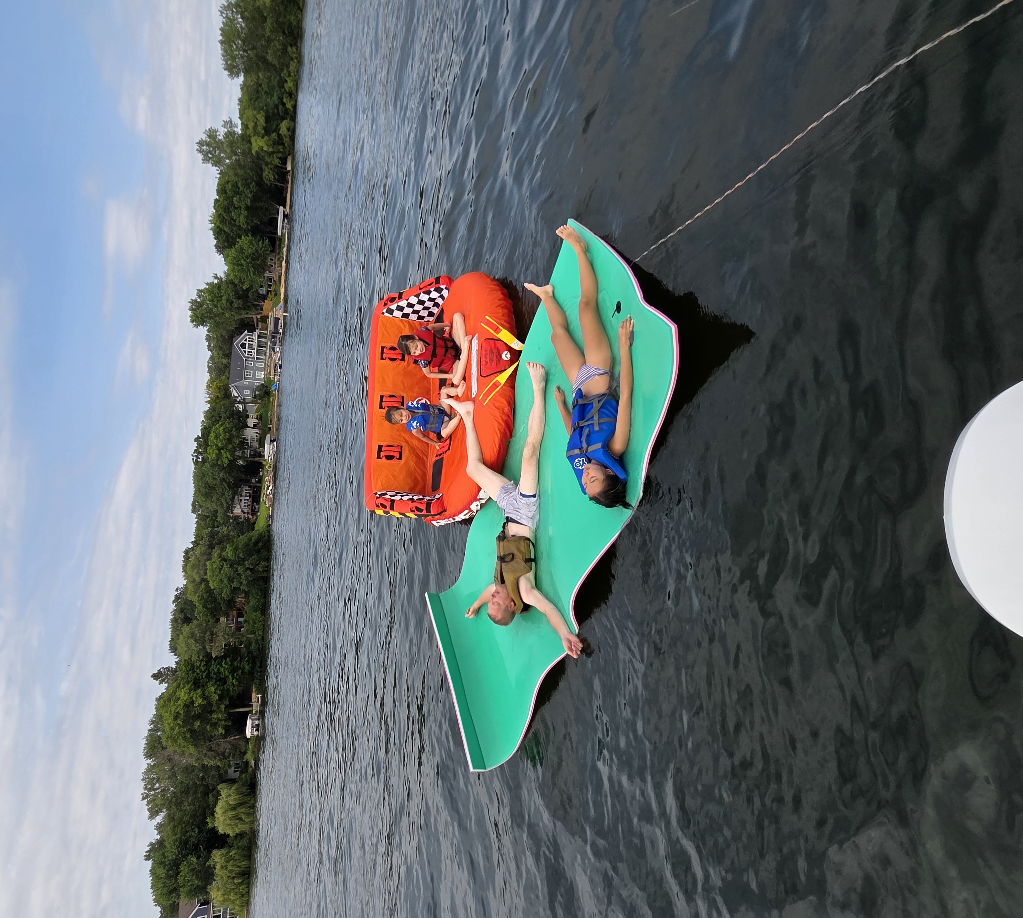 Family relaxing on floating mats and a towable on the lake