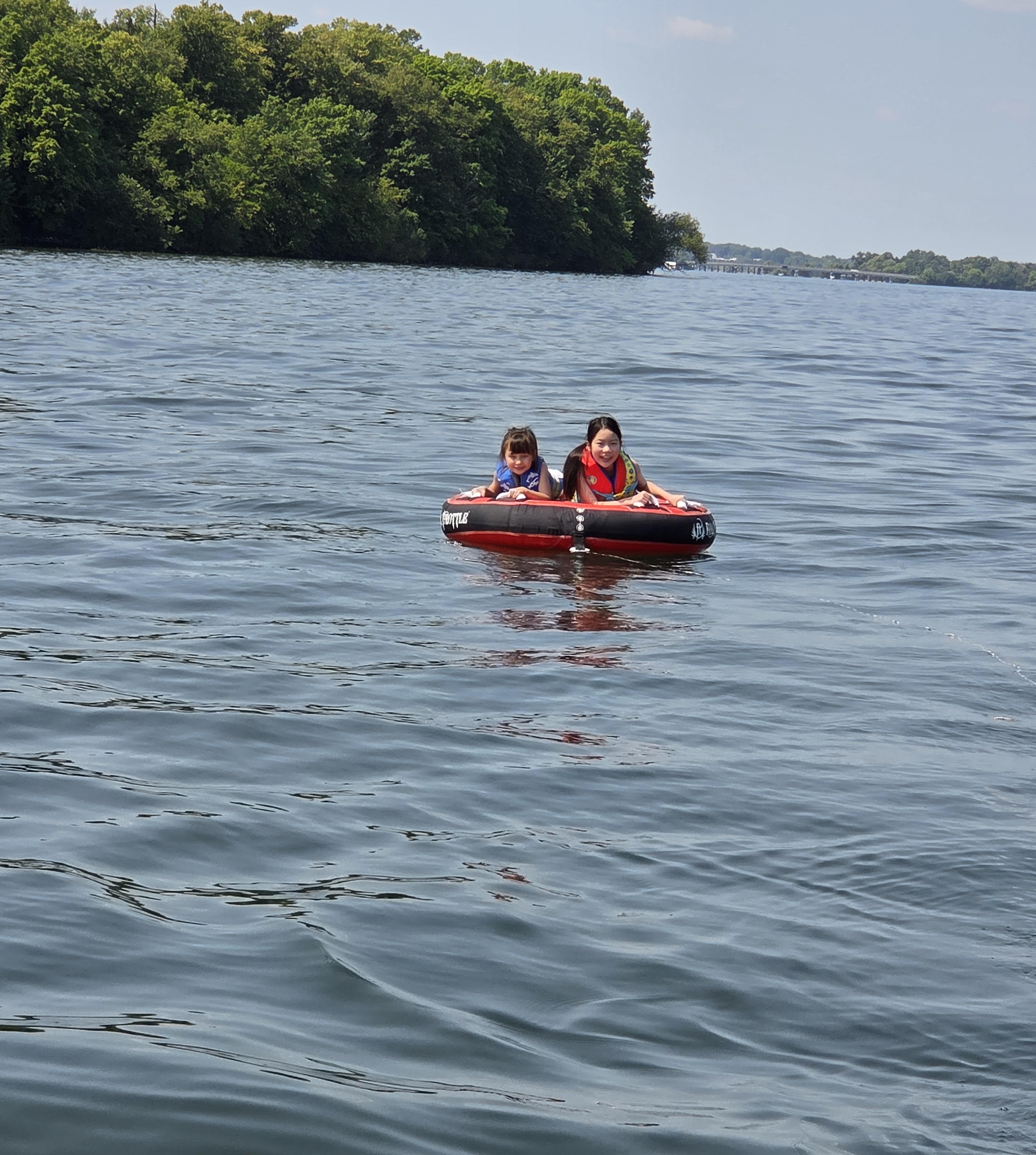 Two children wearing life jackets enjoying a towable tube on the lake